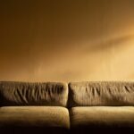 Jesienno-zimowy salon: tekstylia, światło i dodatki, które ocieplają dom Salon z sofą oświetloną ciepłym światłem lampy podłogowej
