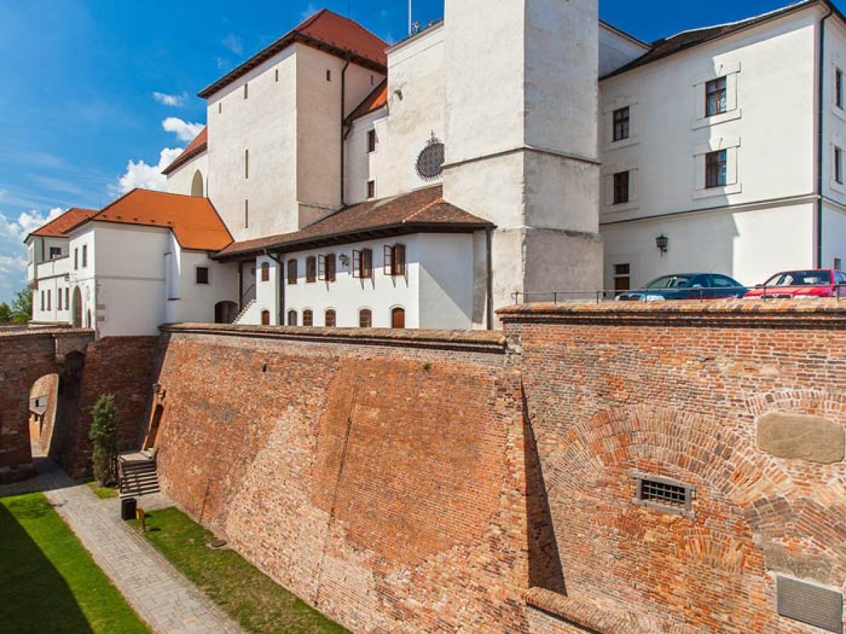Cihlové hradby a bílá věž hradu Špilberk pod modrou oblohou