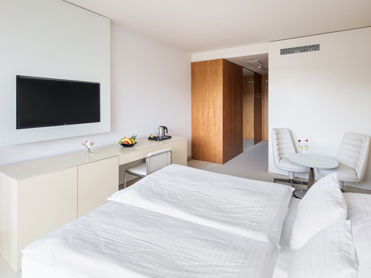 Světlý pokoj v hotelu Thermal s manželskou postelí a posezením u okna