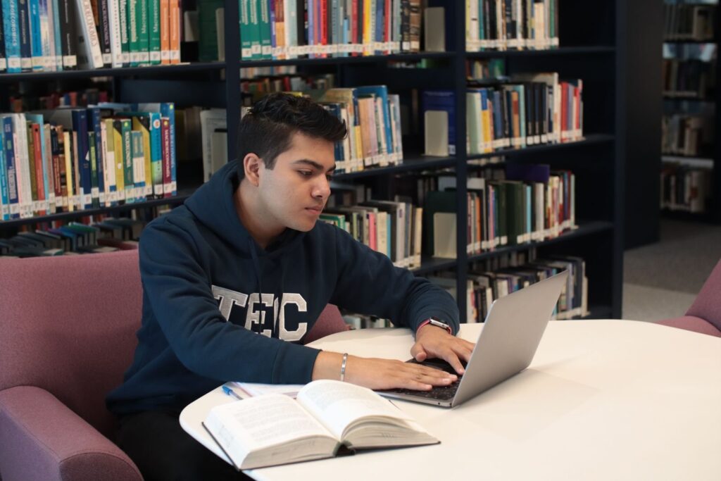 Student pracujący na laptopie w bibliotece wśród książek