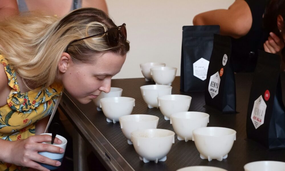 Lidé se sklánějí nad řadou šálků s kávou při degustaci