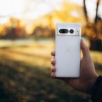 Dłoń trzymająca biały smartfon w jesiennym parku