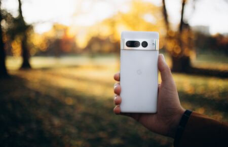 Dłoń trzymająca biały smartfon w jesiennym parku
