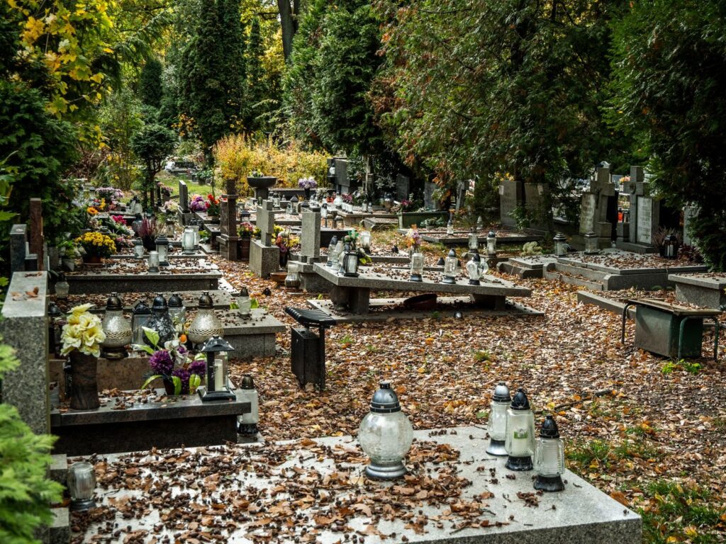 Jesienny cmentarz z opadłymi liśćmi i zniczami na grobach